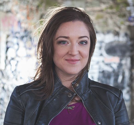 Young woman with brown hair smiling outdoors in a leather jacket.