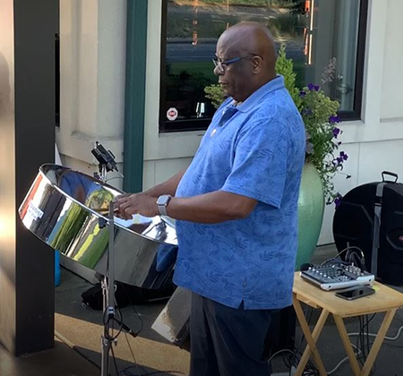 Man playing steel drums outdoors in casual blue shirt.