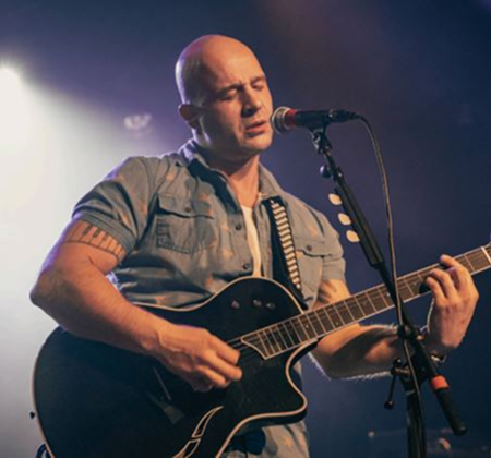 A musician passionately playing guitar and singing on stage under spotlight.