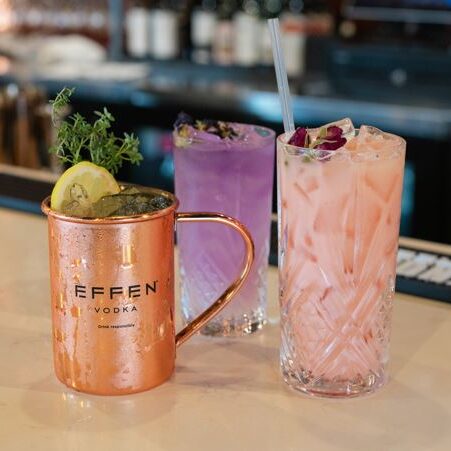 Three colorful cocktails in a bar setting with garnishes.