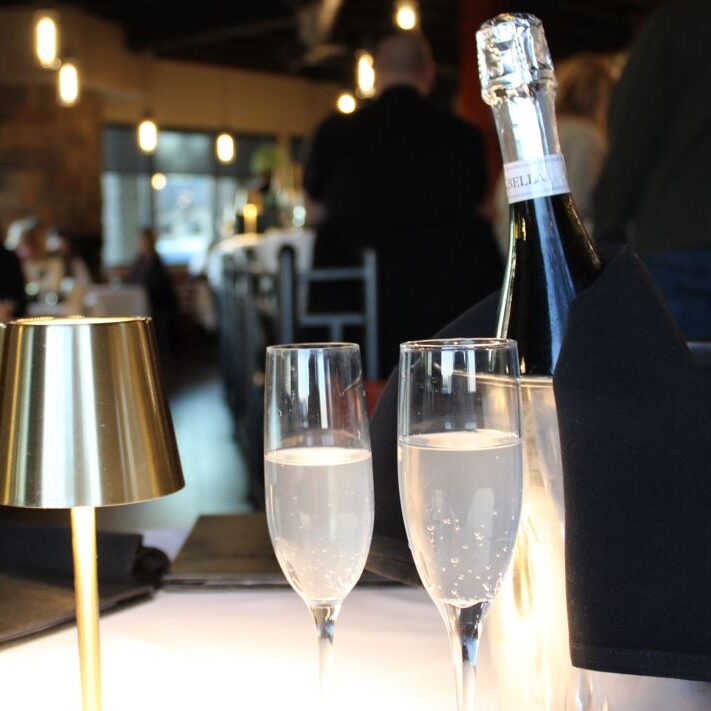 Two champagne flutes with a bottle in a cozy restaurant setting.