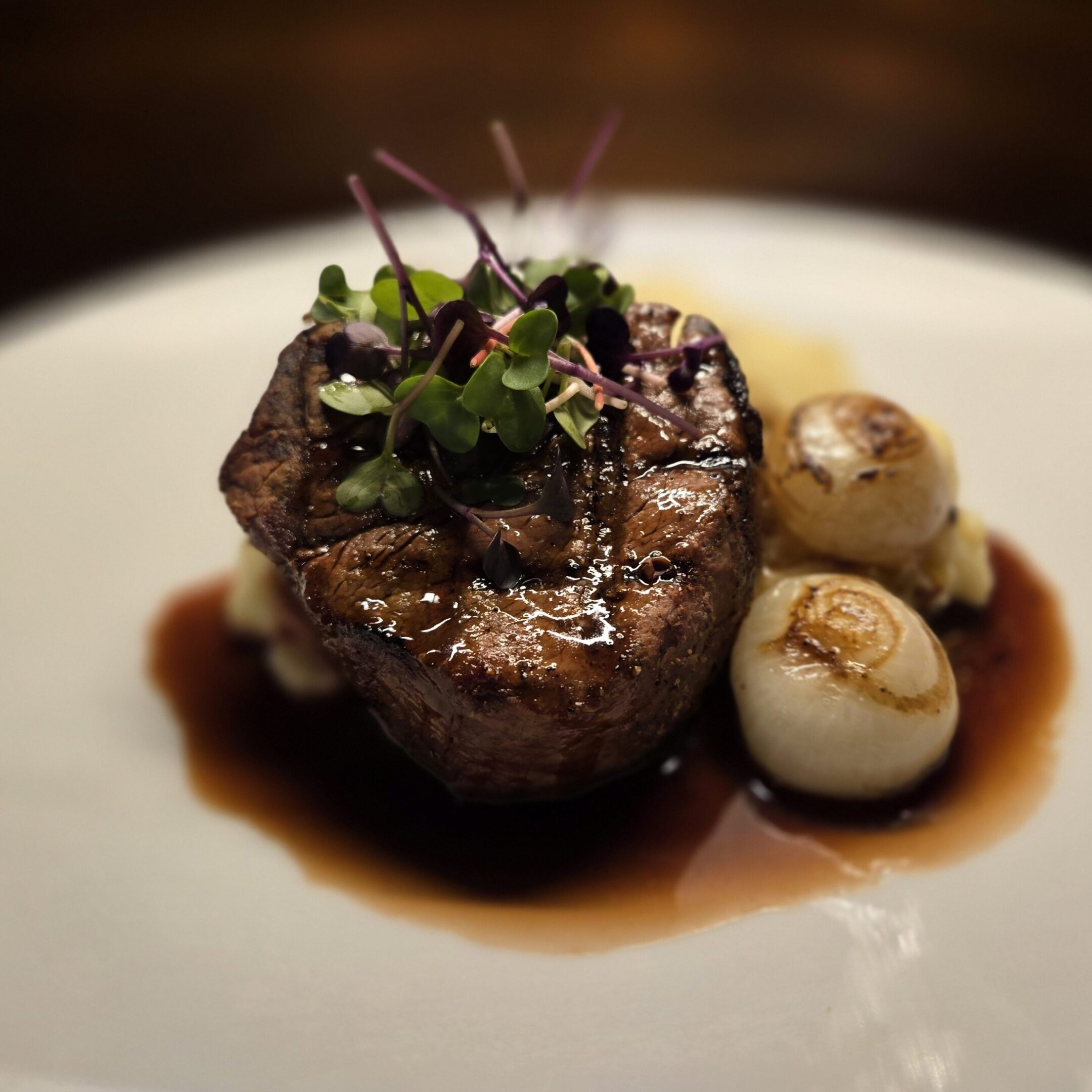A gourmet steak with sauce and roasted garlic cloves on a white plate.